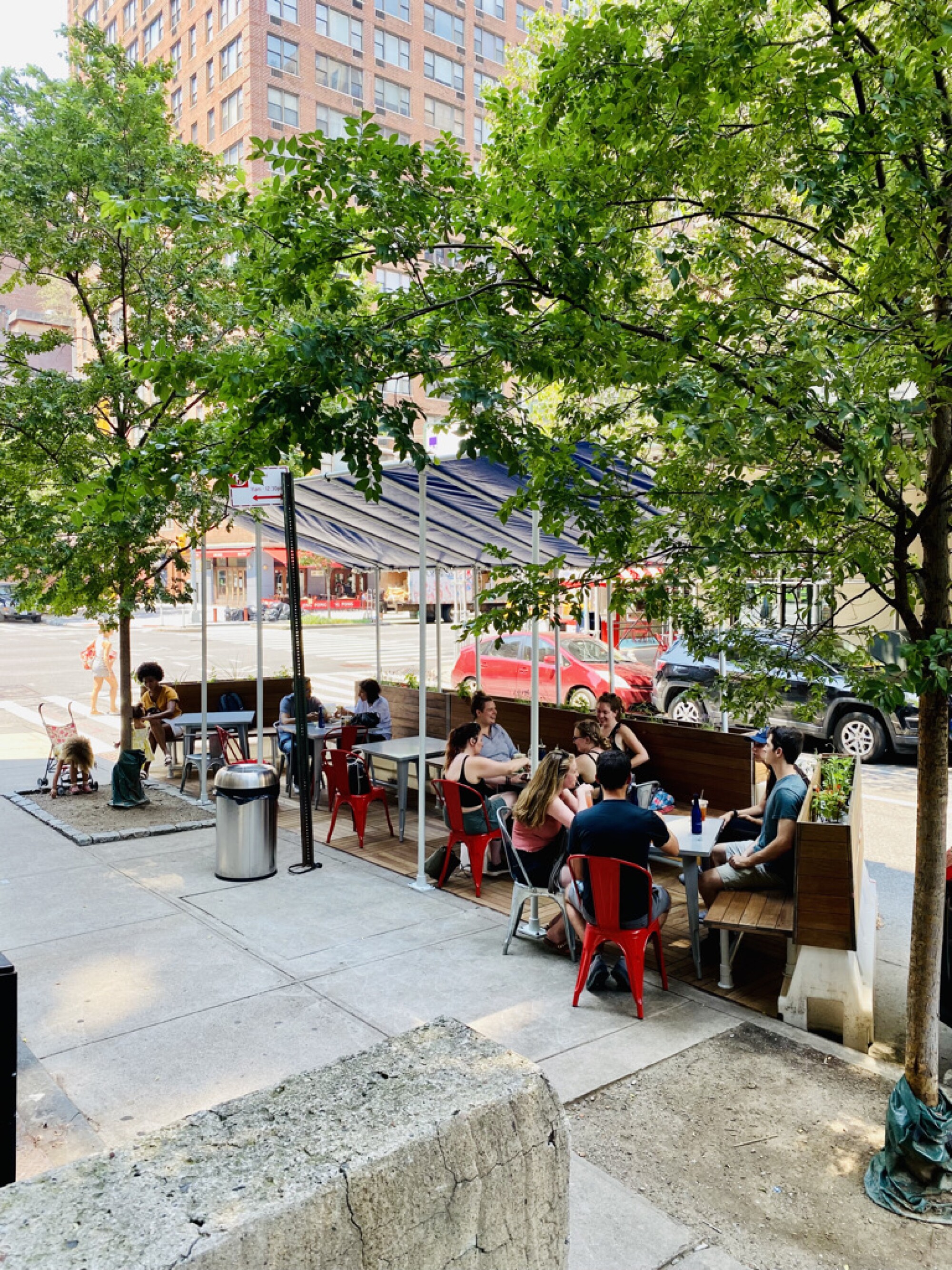 People sit on shaded benches in a small parklet contained within water barriers