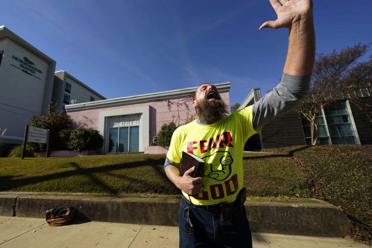 A man in a "Fear God" T-shirt speaks with his hand raised outside an abortion clinic.
