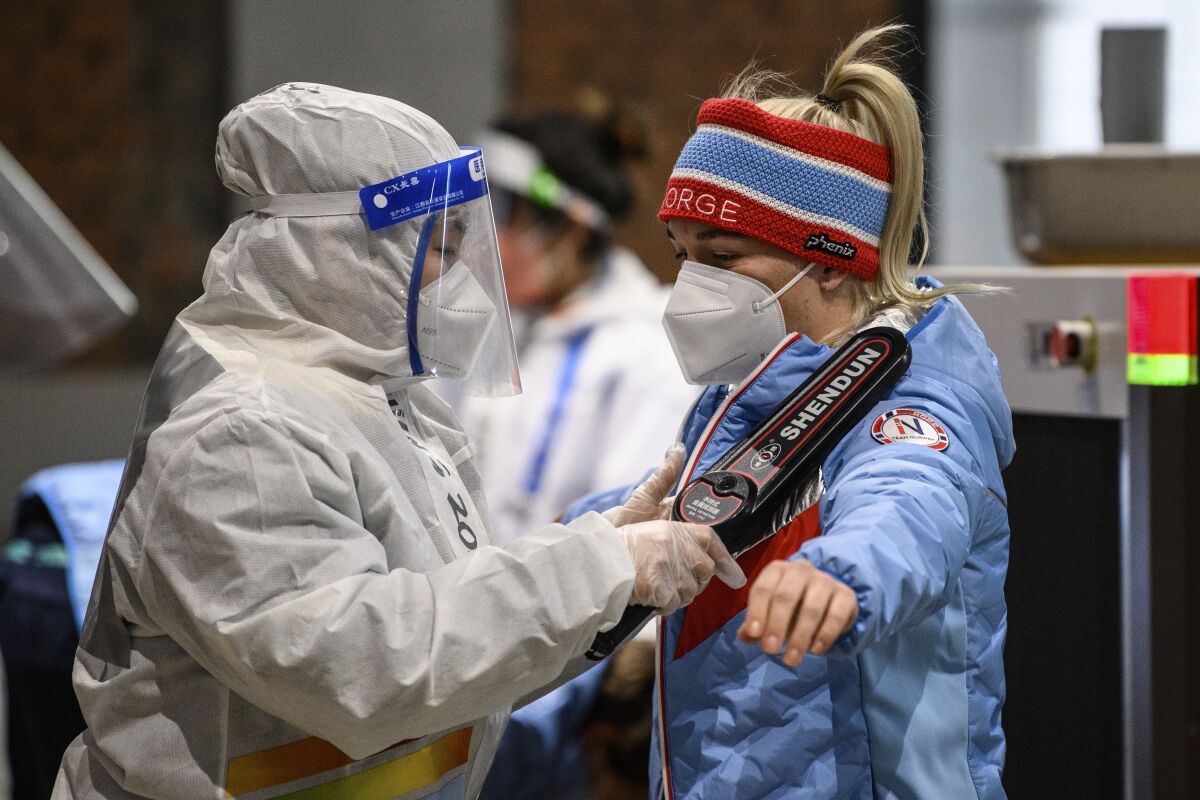 A person in a hazmat suit uses a wand to scan a member of the Norway delegation at the 2022 Olympics.