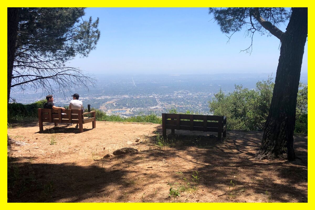 Two people sit talking on a bench at Henninger Flats, with a view overlooking the city below.