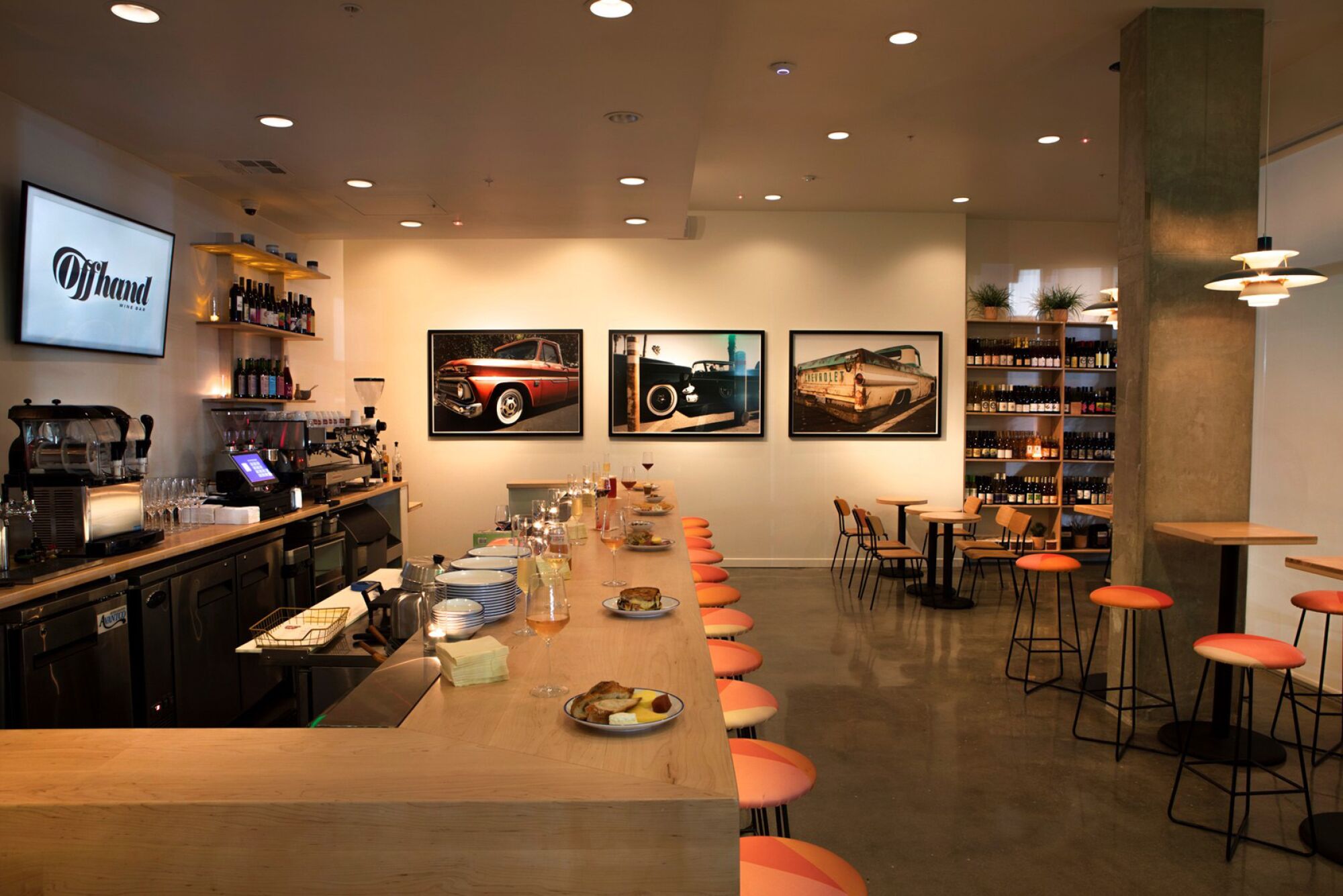 A bar with orange geometric stools and framed pictures of vintage cars