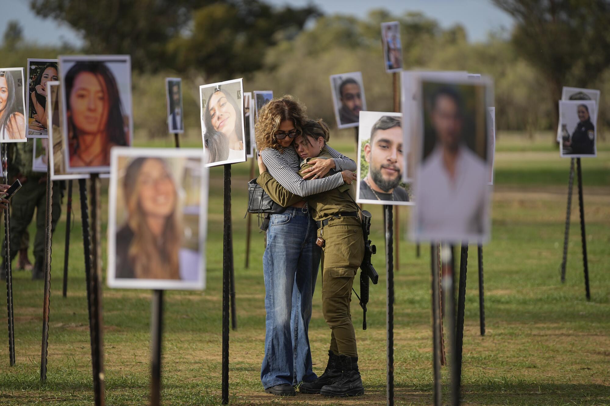 Two people, one in military uniform and armed, embrace amid photos of people elevated on poles