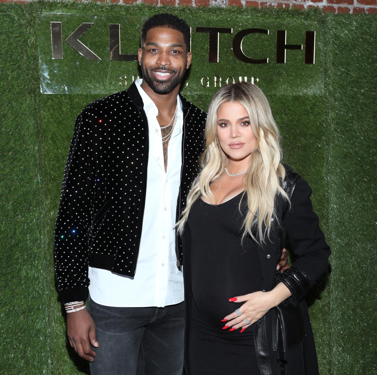 A tall man and a pregnant woman pose together at an event
