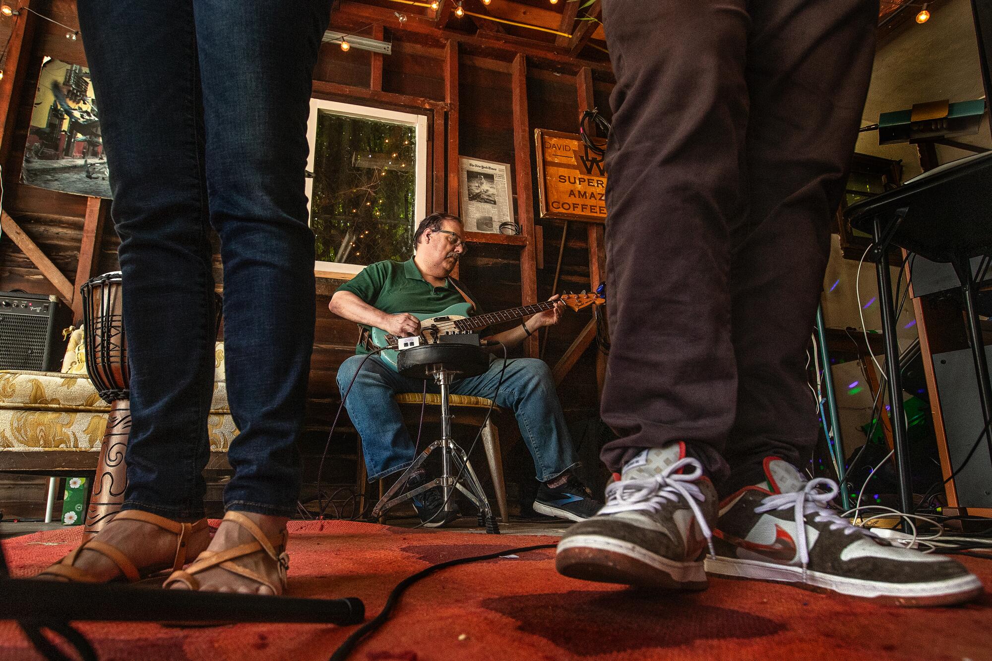A man playing the guitar is visible between two pairs of feet on the floor.