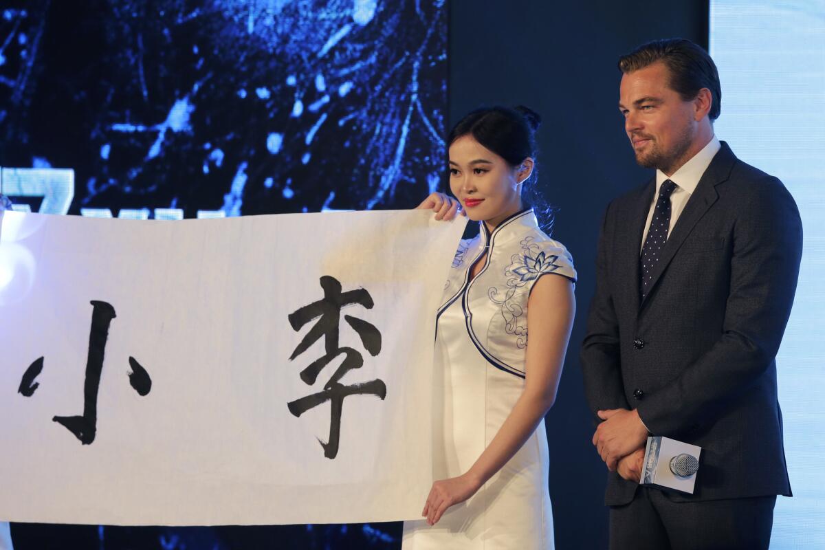 Leonardo DiCaprio with a hostess holding a paper bearing Chinese characters he wrote during a news conference for the movie “The Revenant” in Beijing, March 20, 2016.