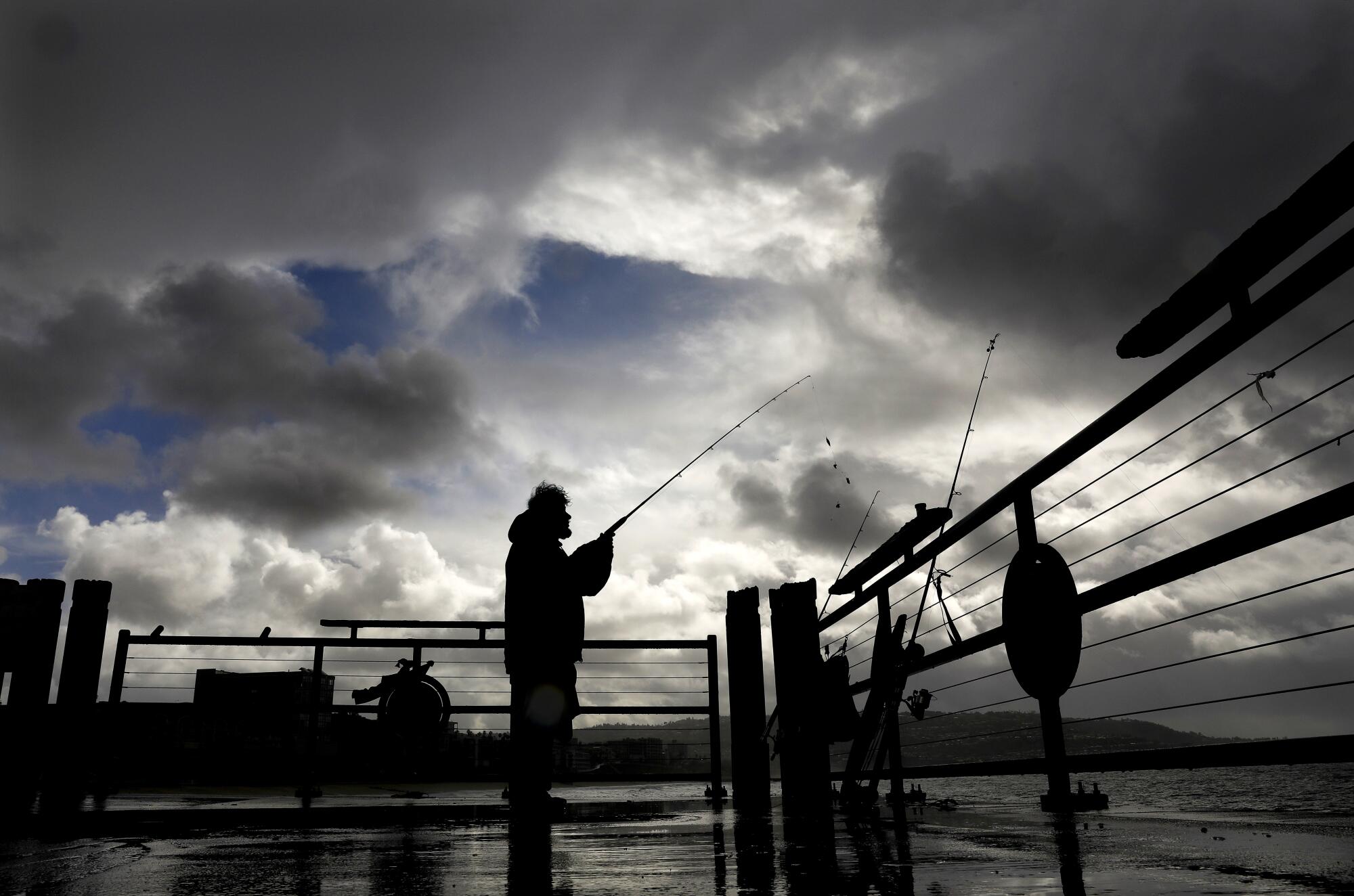 Dark clouds hang over a fisherman on a pier.