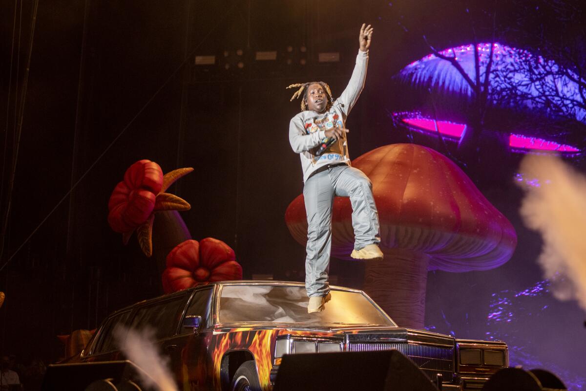 Hip-hop artist Don Toliver jumps in the air on a stage decorated with a flame-painted limo and giant psychedelic mushrooms.