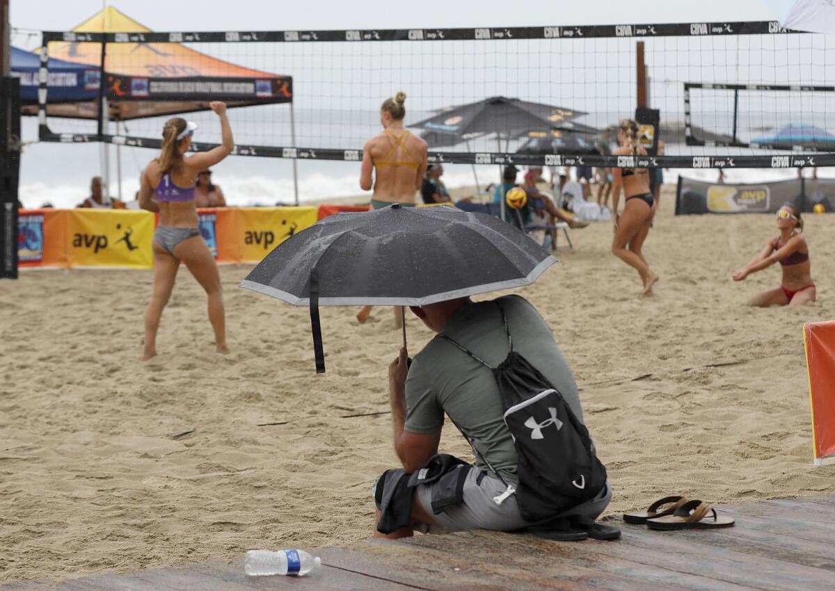 A spectator leans under an umbrella as rain begins to fall at the Laguna Open women's beach volleyball match on Friday.