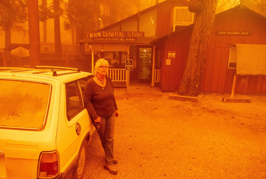 A woman leans against a car under an orange sky.