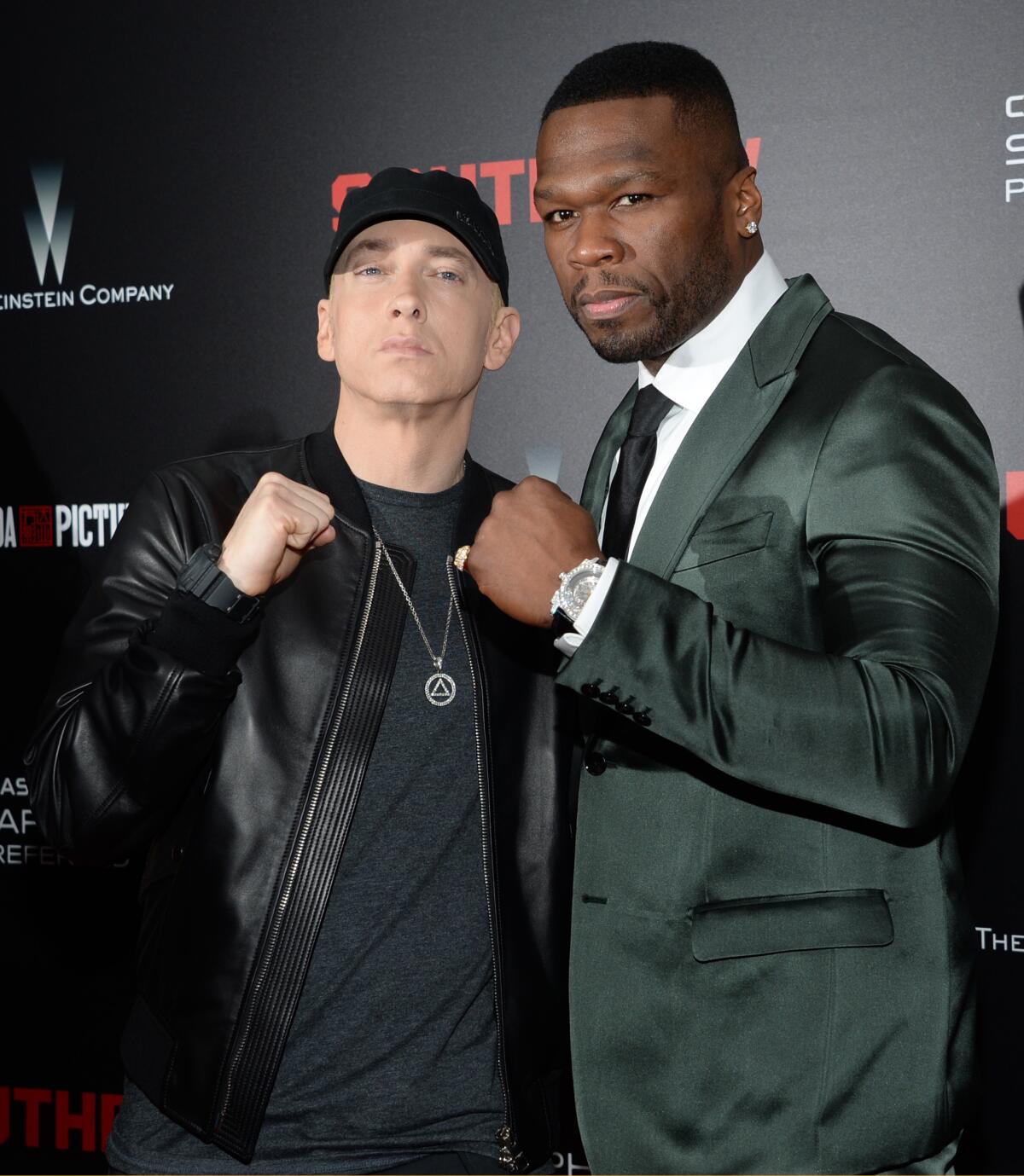 Eminem and 50 Cent each raise a fist as they pose together with serious faces