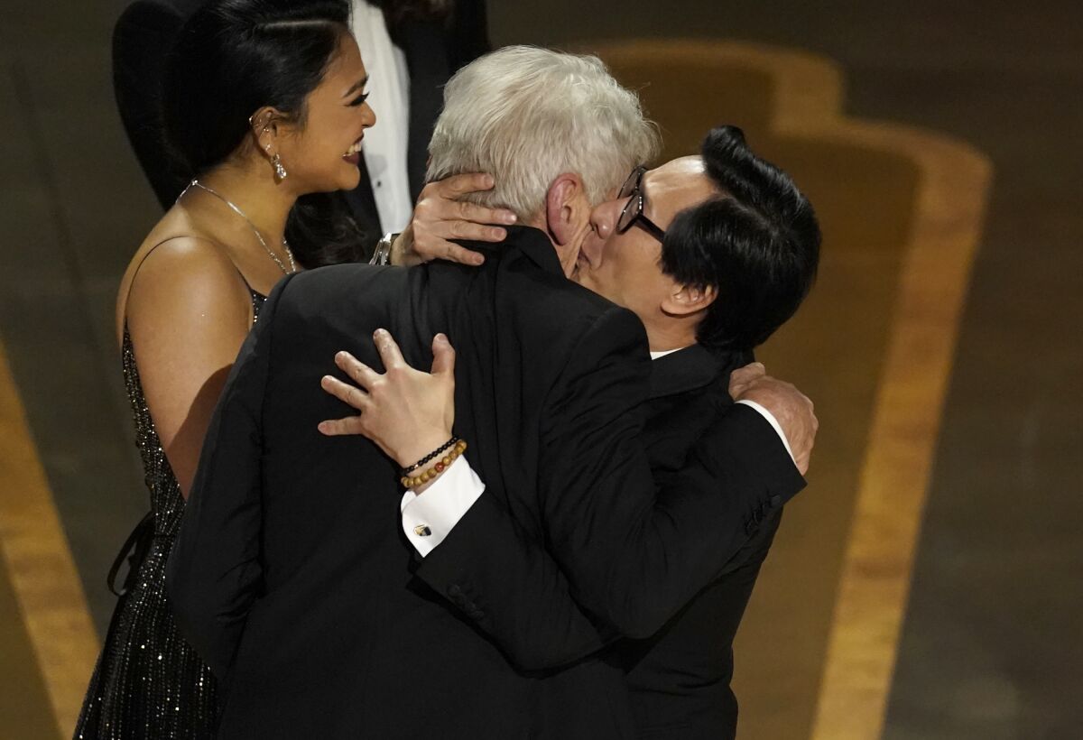 Two men in suits sharing a tight embrace on a stage