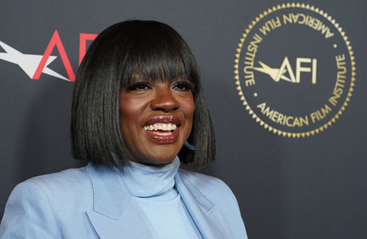 A woman with short hair smiles in a powder blue shirt and blazer