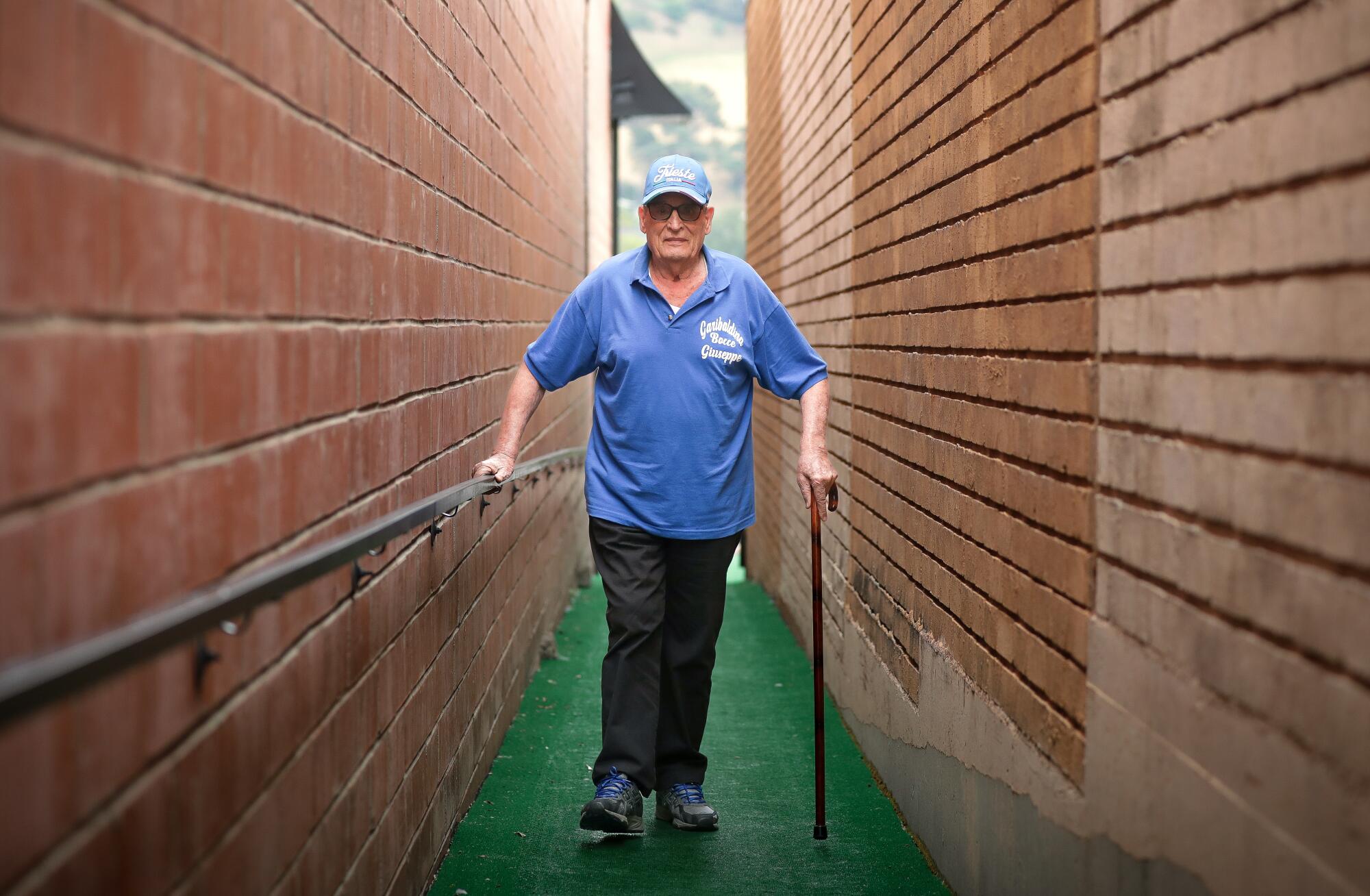 A man walks along a pathway between brick walls to play bocce ball.