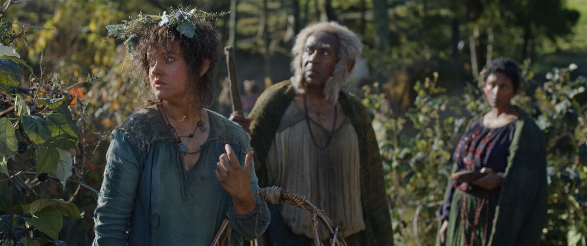 A young woman with plants in her hair standing near a man and another woman.