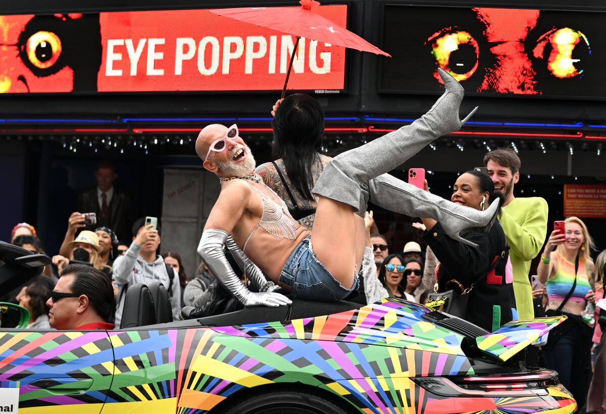 An L.A. Pride parade participant rides on a car along Hollywood Boulevard