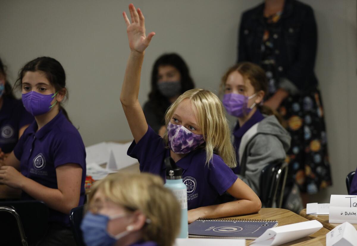 A masked student raises a hand in class.