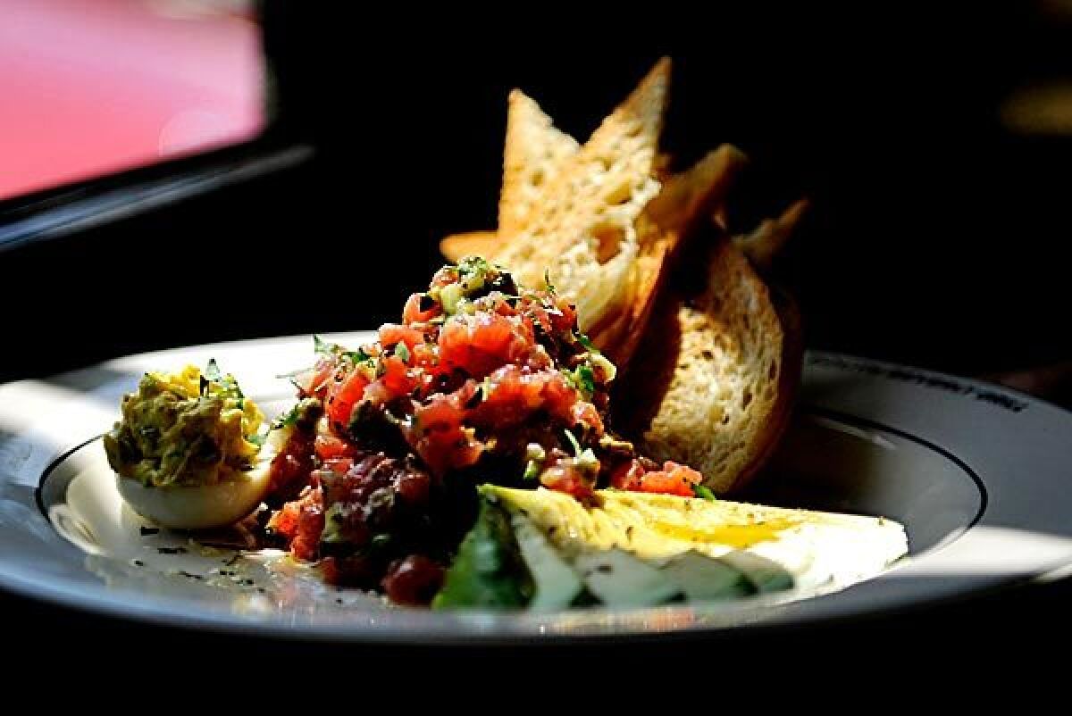 Ahi tuna tartare is served with a stack of thin toasts and a fan of avocado.