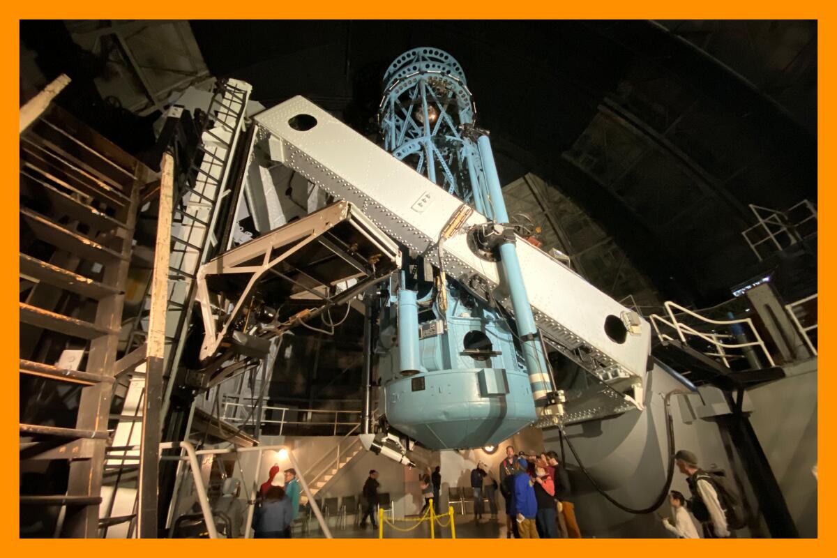 A large green cylindrical telescope supported by even larger, white metal arms in the middle of a domed roof.