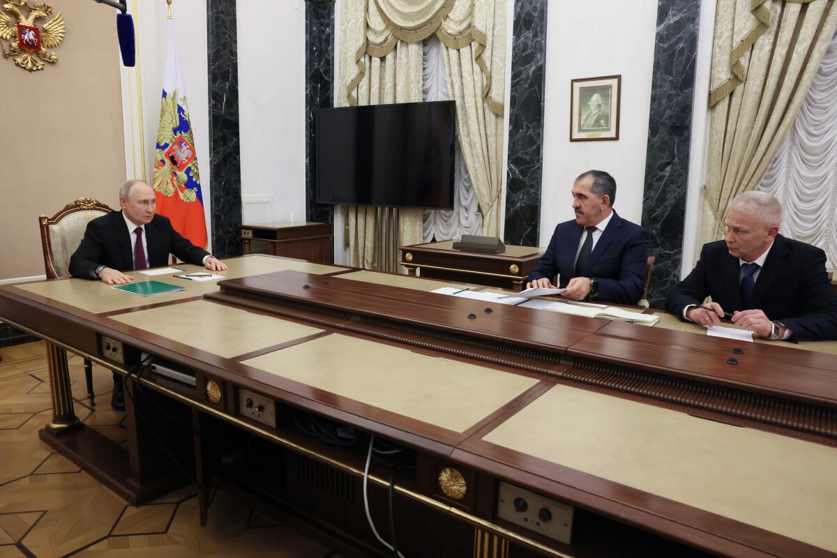 Russian President Vladimir Putin at a table with two other officials