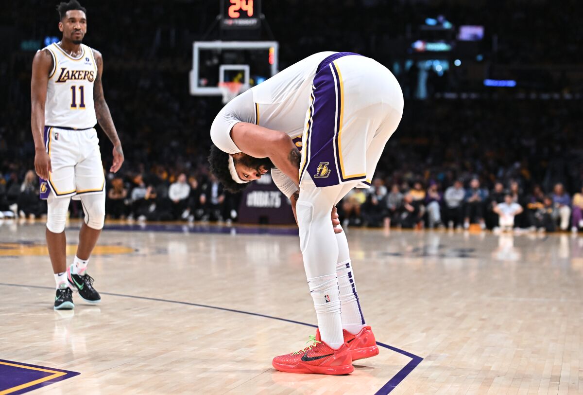 Lakers forward Anthony Davis bends over and holds his right leg.