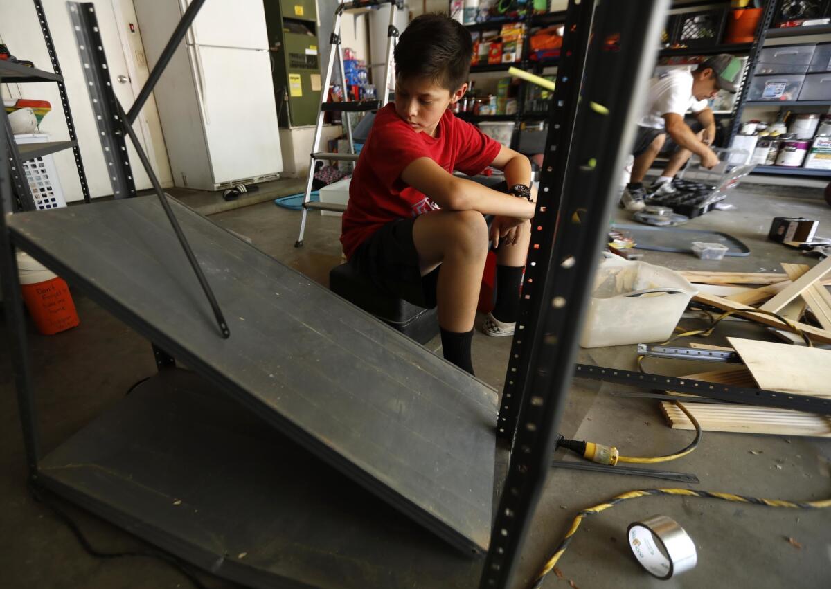 Joaquin Vasquez, 12, looks over earthquake damaged shelves as his father, Alex Vasquez, cleans up their garage in Ridgecrest. "We lucked out. We didn't get much damage," Alex said.