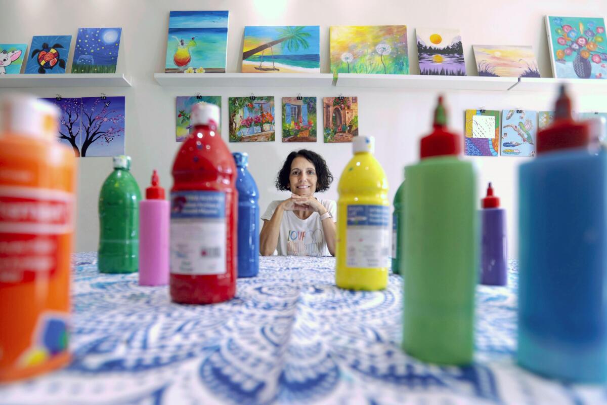 Ronit Rozen is surrounded by some of her paintings and bottles of paint used at her studio The Artsy Backyard.