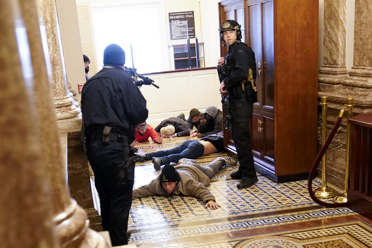 People lie facedown on the floor of the Capitol as police stand over them with weapons.
