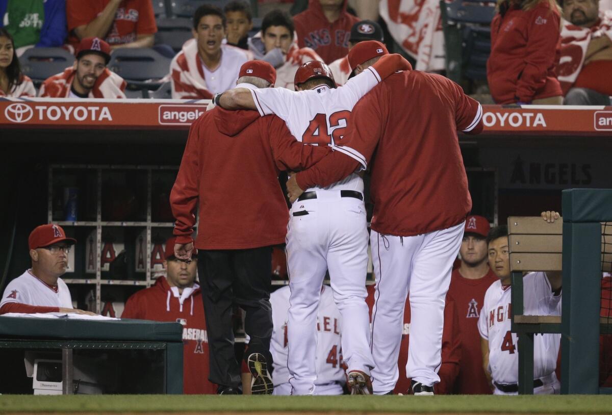Kole Calhoun, center, is helped off the field by Manager Mike Scioscia, right, and assistant athletic trainer Rick Smith during the 11th inning of the Angels' 10-9 loss to the Athletics.