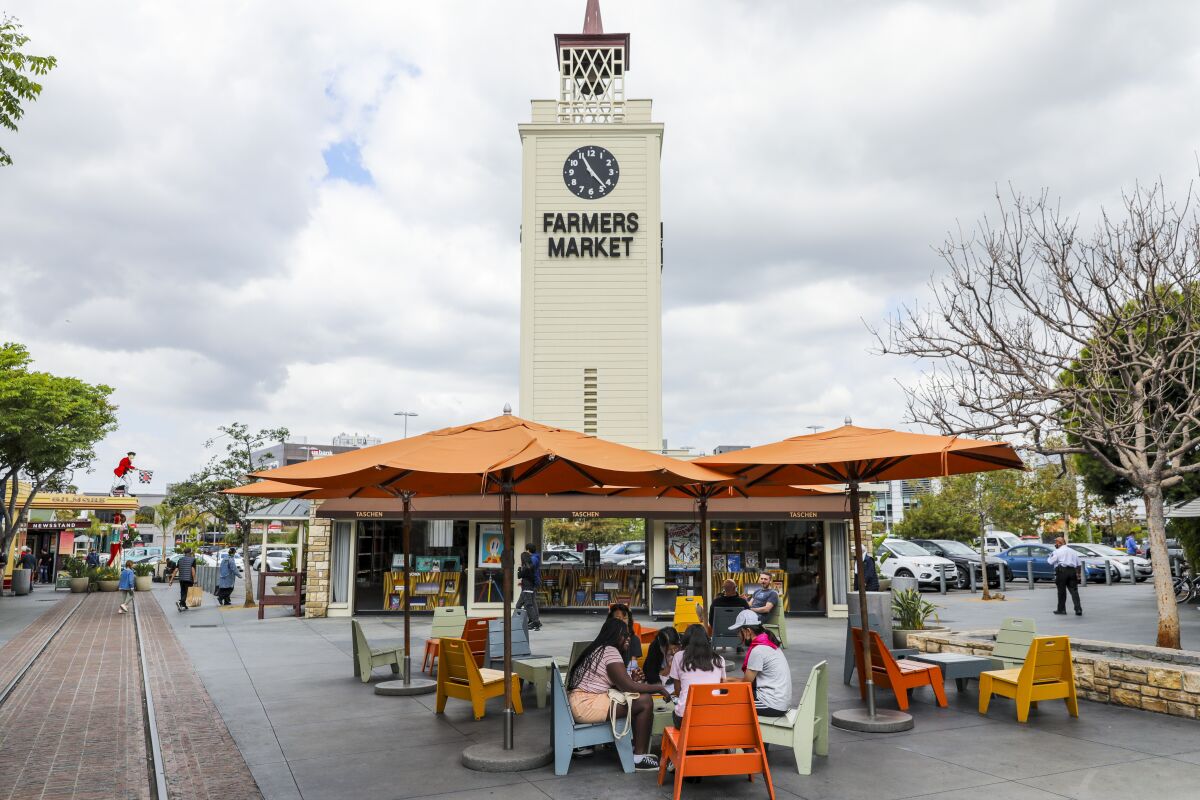 A clock tower with the words Farmers Market on it above a cluster of umbrella-covered tables