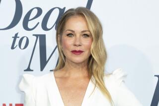 Christina Applegate in a white V-neck dress wearing red lipstick and posing against a white background with black text