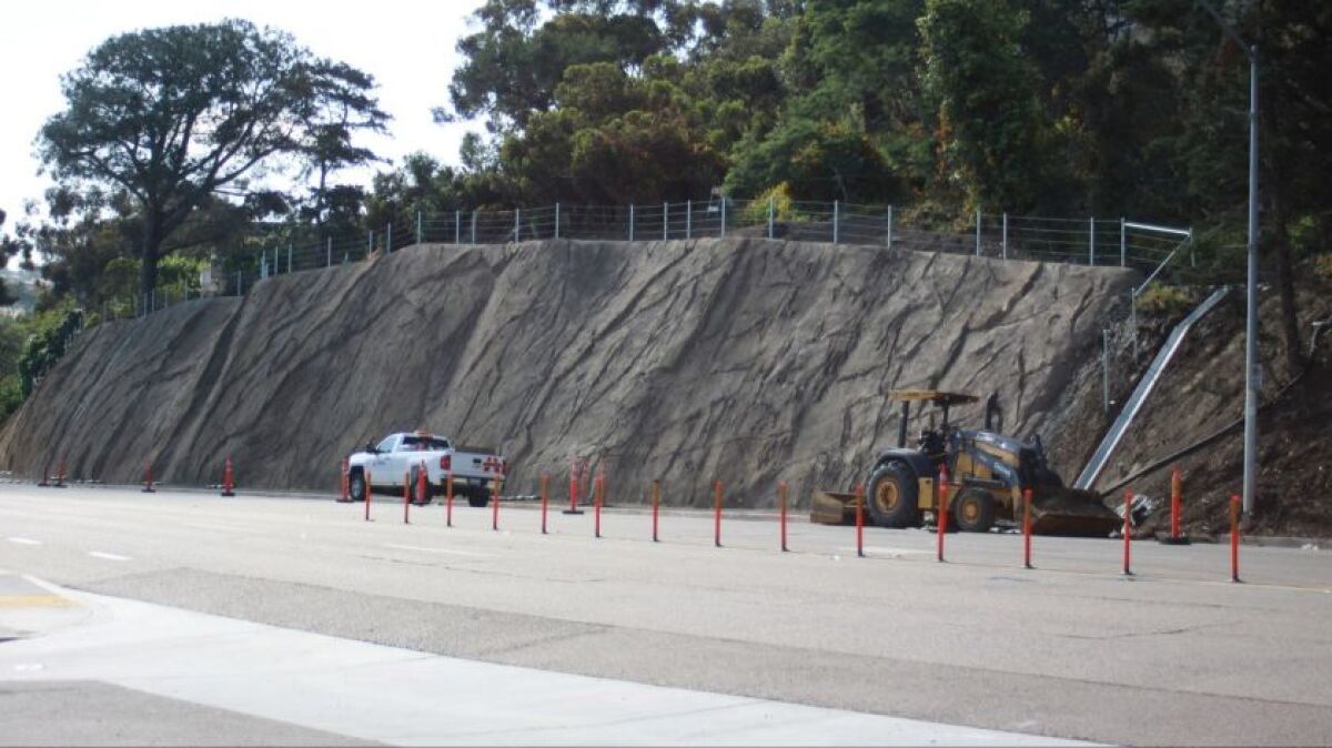 Construction bollards and equipment below an exposed slope alongside a roadway