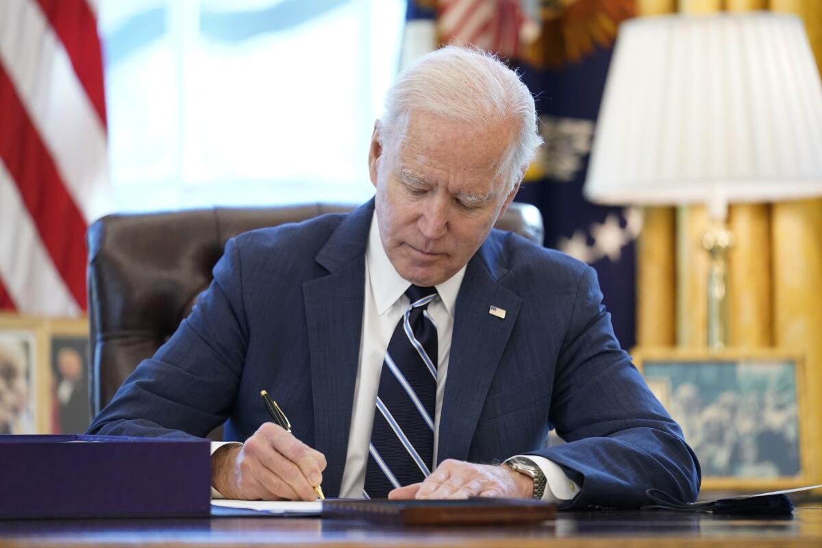 Biden sits at a desk with pen in hand