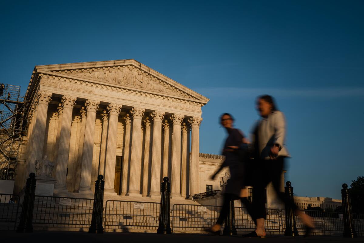 The Supreme Court building at sunset as two people walk by in the foreground. 