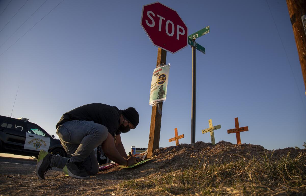A man kneels to place wooden crosses in the dirt