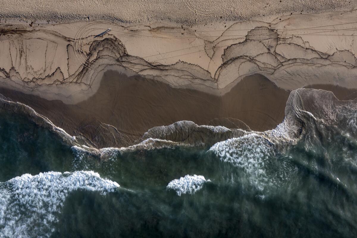 An aerial view looking down at dark marks and waves on a beach.