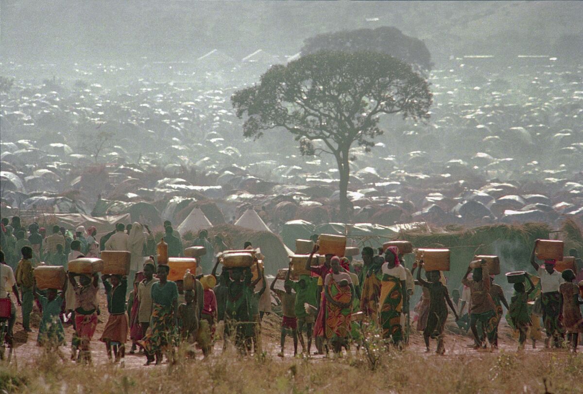 FILE - In this Tuesday, May 17, 1994 file photo, refugees who fled the ethnic bloodbath in neighboring Rwanda carry water containers back to their huts at the Benaco refugee camp in Tanzania, near the border with Rwanda. A report commissioned by the Rwandan government due to be made public on Monday, April 19, 2021 concludes that the French government bears "significant" responsibility for "enabling a foreseeable genocide" that left more than 800,000 dead in 1994 and that that France "did nothing to stop" the massacres. (AP Photo/Karsten Thielker, File)