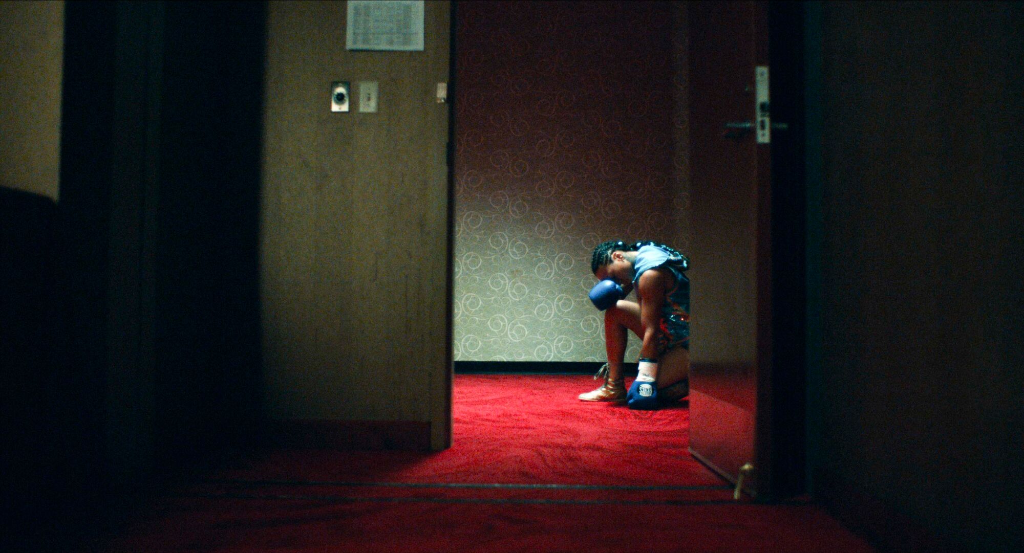 A female boxer, seen through an open door, hunches over.