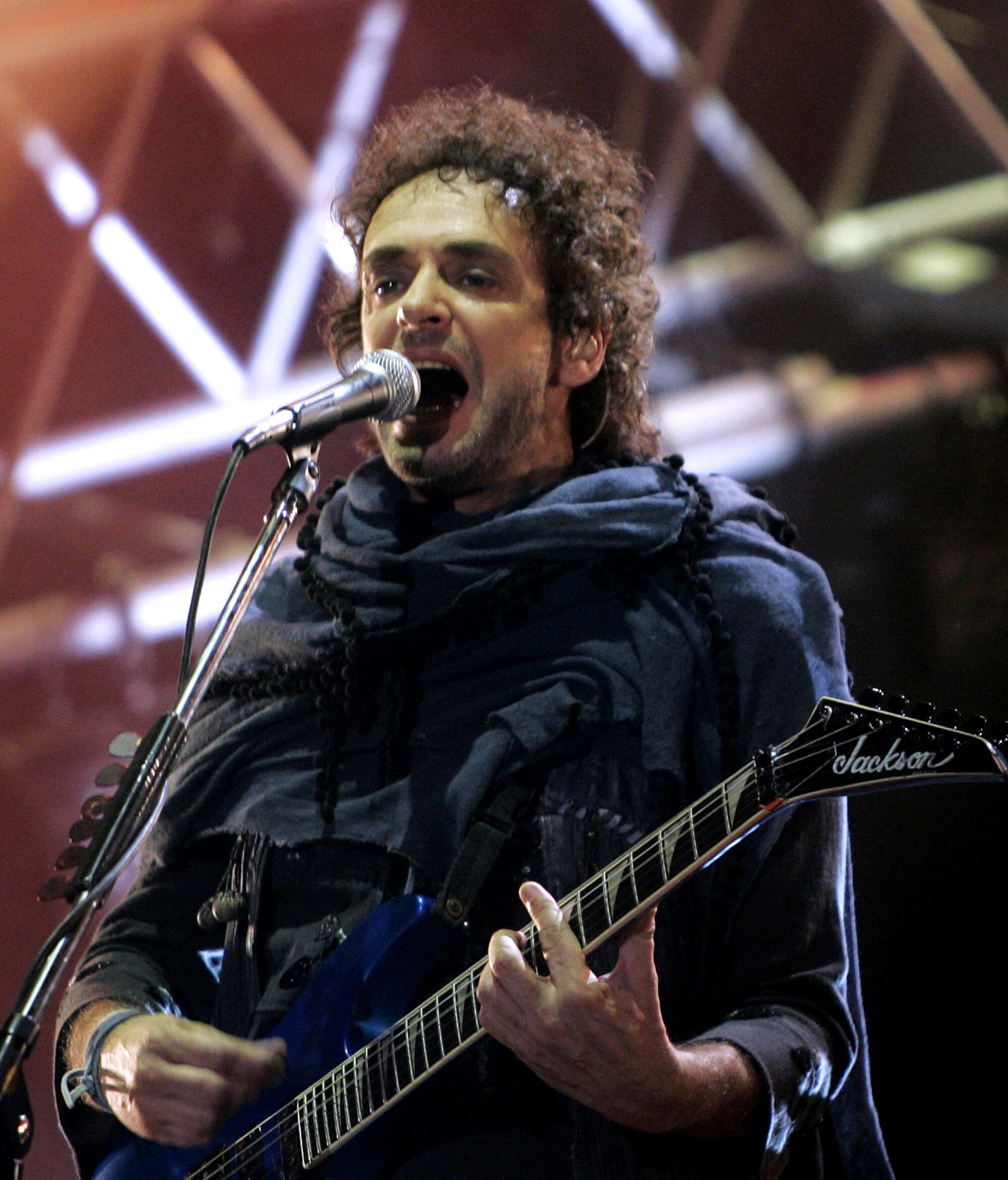 A man with dark curly hair plays guitar and sings into a microphone onstage