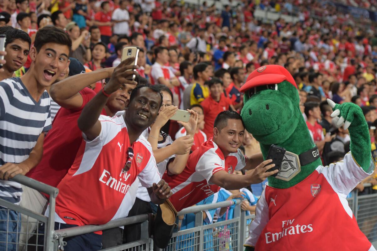 Fans pose for pictures with Arsenal's mascot Gunnersaurus  