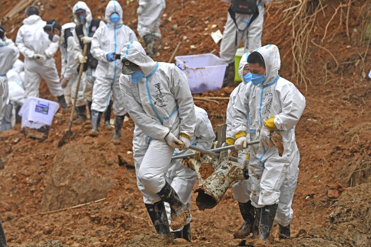 White-suited searchers carrying piece of crashed plane