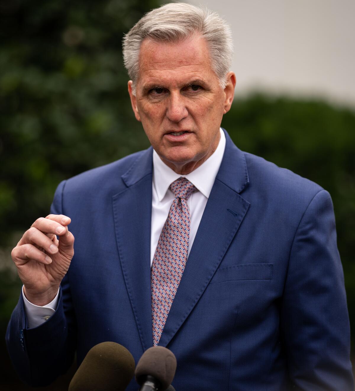 A man with his hand raised in front of microphones.