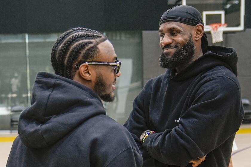 Bronny and LeBron James smile while standing and looking at each another on the court at the Lakers practice facility