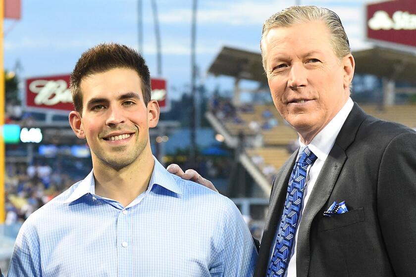 Dodgers broadcasters Joe Davis and Orel Hersheiser pose on the field together before a game.