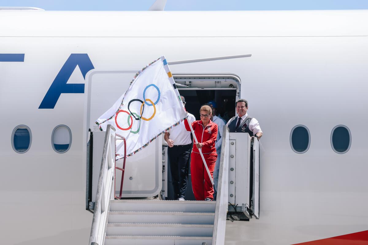 A woman holds the Olympic flag atop an airline stairway.