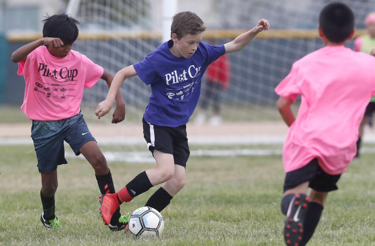 Carden Hall's Truman Kemp, center, dribbles the ball against Newport in a boys' fifth- and sixth-grade Bronze Division pool-play match at the Daily Pilot Cup on Friday at Costa Mesa High.