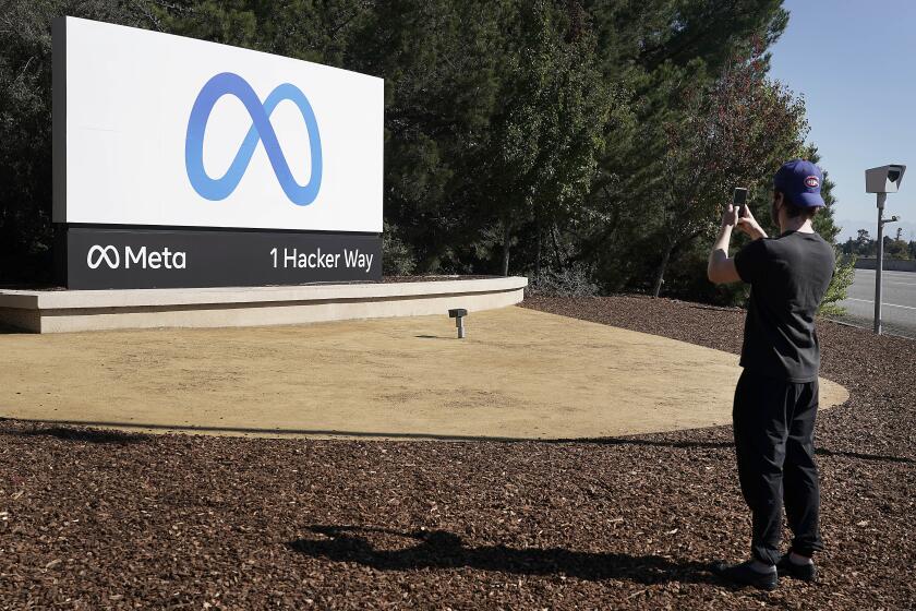 A man takes a picture of the Meta logo on a large roadside sign at the entrance to the company's headquarters