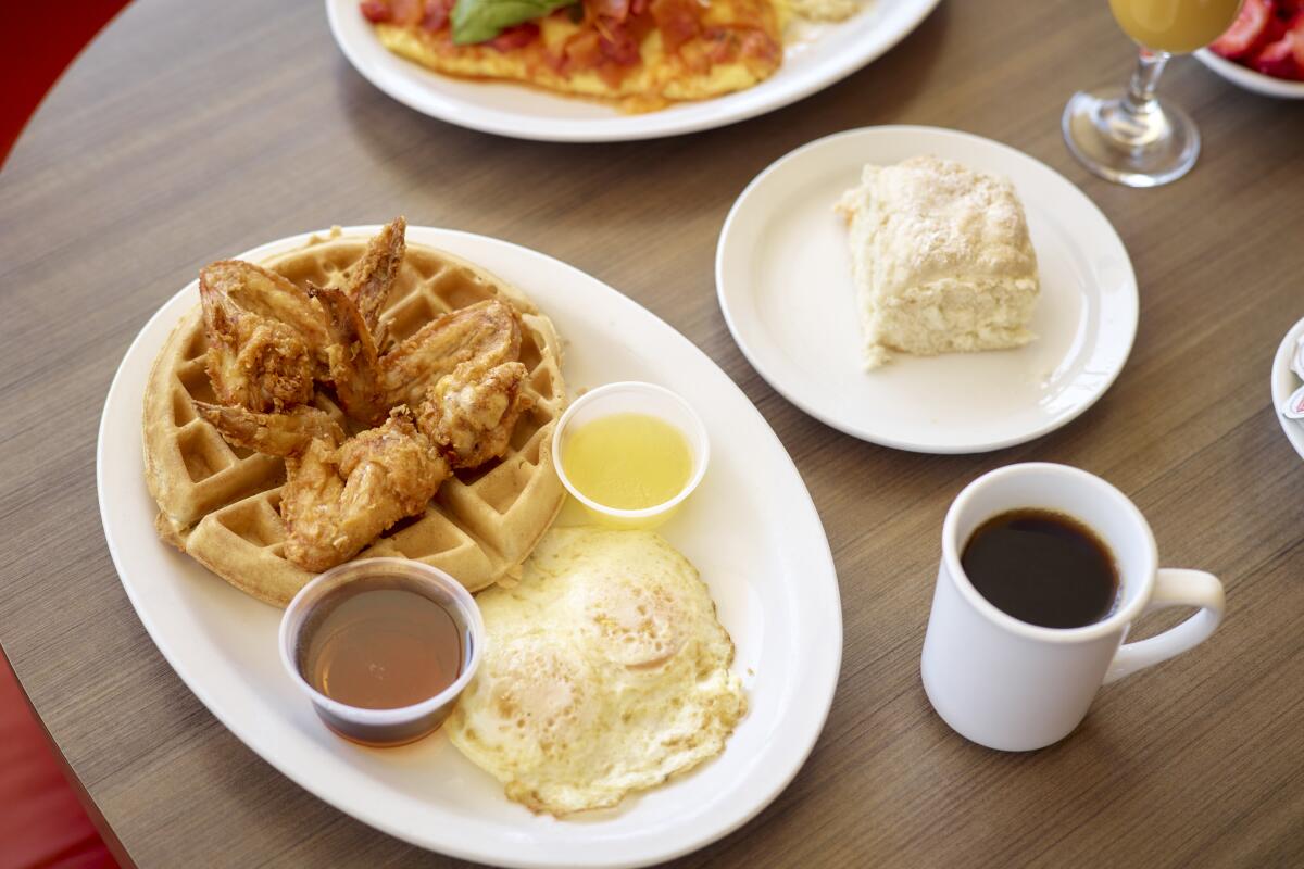A plate with chicken, waffles and eggs on a table with a mug of black coffee