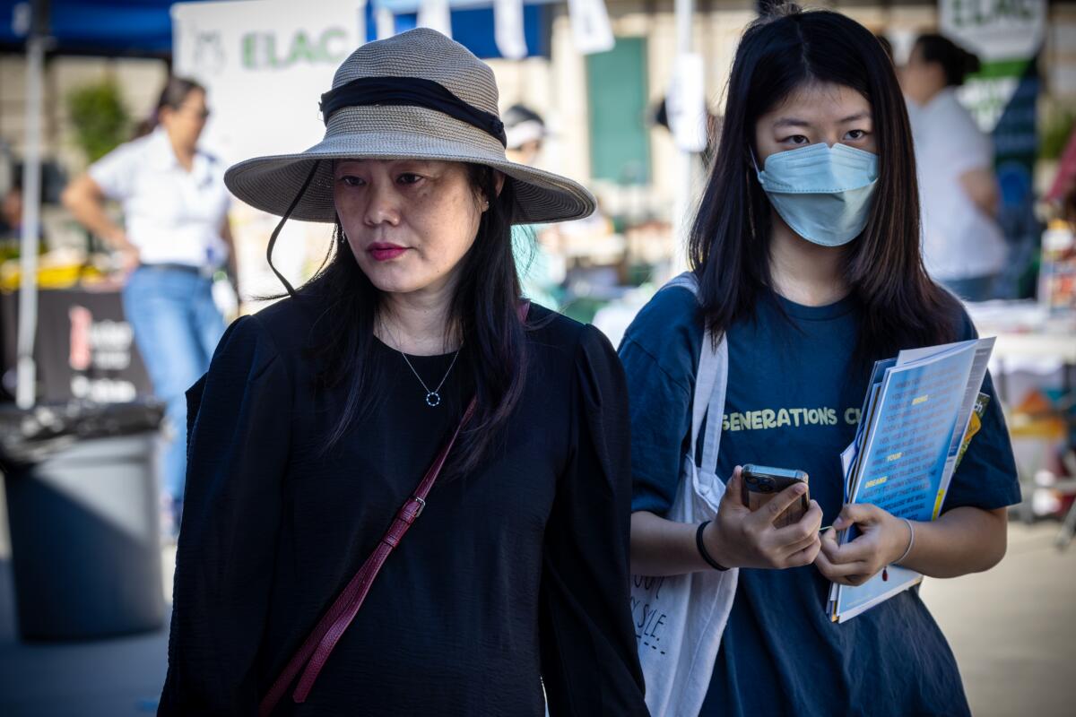 A woman stands next to her teenage daughter, who is wearing a mask.