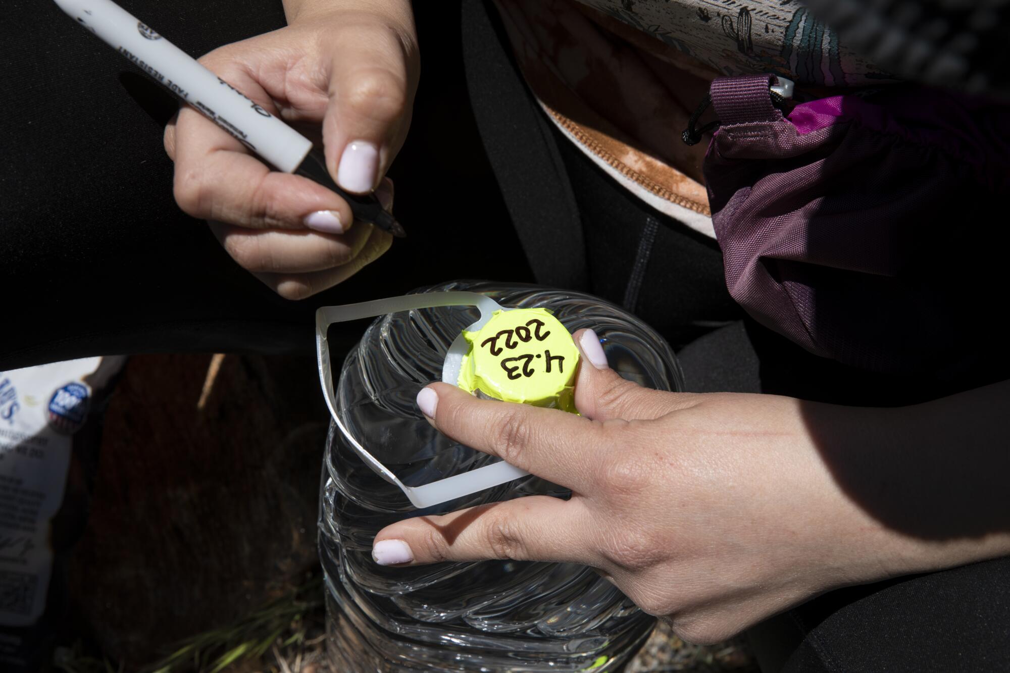 Armida Gomez, 34, writes the date on newly delivered 2-gallon bottles of water.