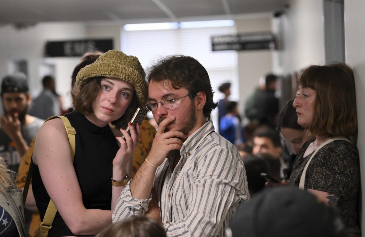 Two people, in a crowd at a city hall, listen to a phone. 